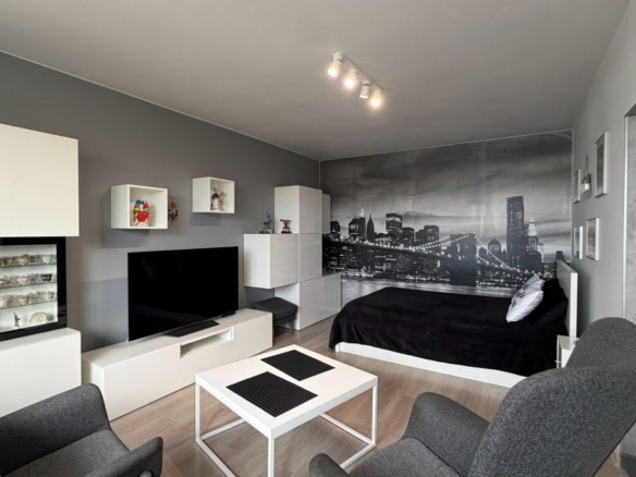 Modern studio with white modular furniture, gray walls, and a black bed against a city skyline mural at the far wall.