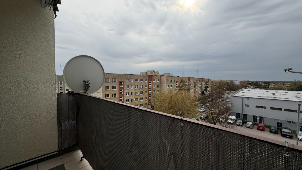 Balcony with a satellite dish overlooking a row of apartment buildings and a parking lot under a cloudy sky