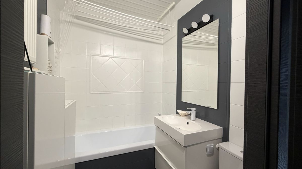 Small modern bathroom with white tiled walls, dark accent wall, rectangular mirror, white sink vanity, toilet, and bathtub.