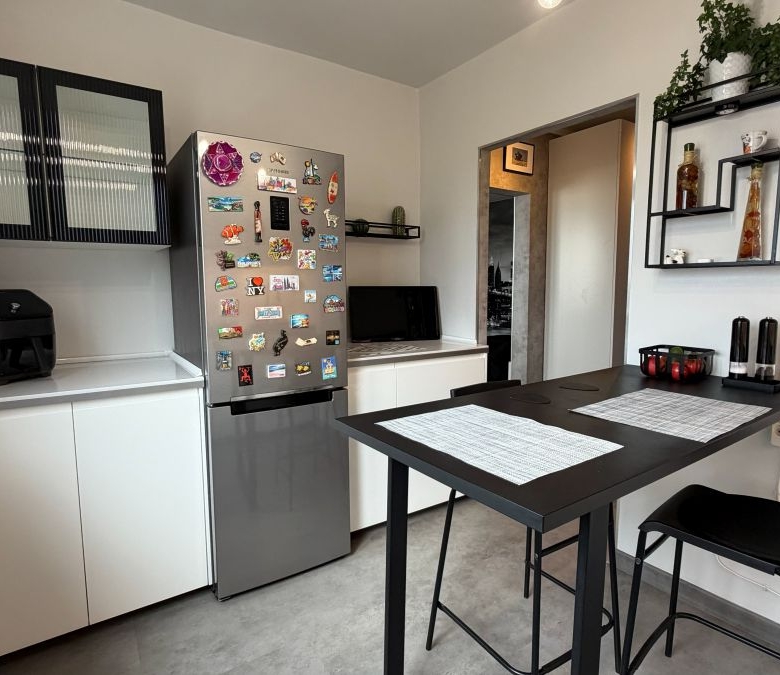 Compact kitchen with white cabinets, a magnet-plastered stainless fridge, and a black dining table with two placemats.