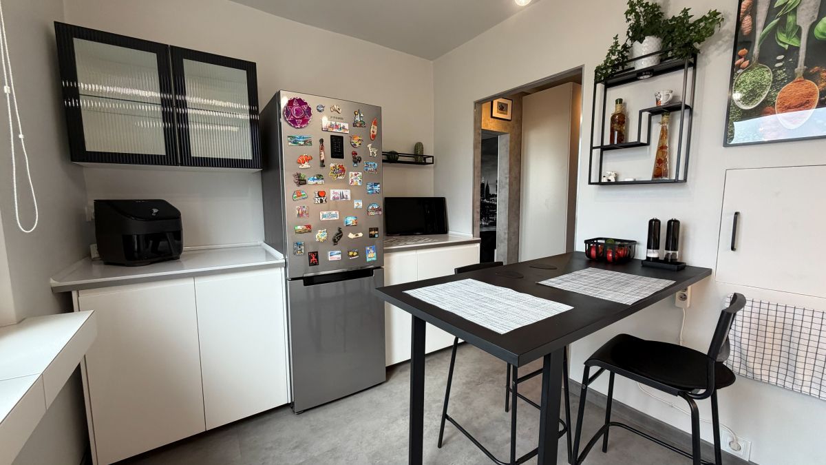 Compact kitchen with white cabinets, a magnet-plastered stainless fridge, and a black dining table with two placemats.