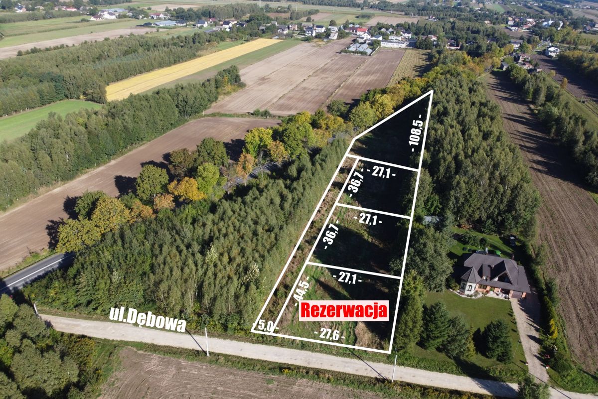 Aerial view of a triangular land parcel outlined with white borders, along Ul. Dębowa, with measurement labels and a red 'Rezerwacja' banner indicating reserved status.