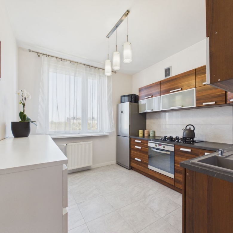 Modern kitchen with wooden cabinets, stainless fridge, oven, and gas stove; white countertops and a double sink under a window.