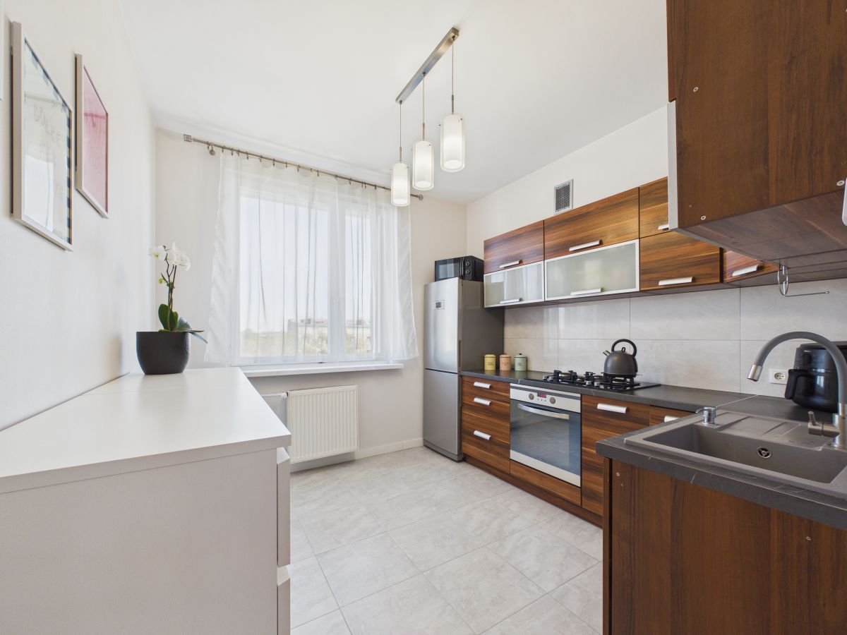 Modern kitchen with wooden cabinets, stainless fridge, oven, and gas stove; white countertops and a double sink under a window.