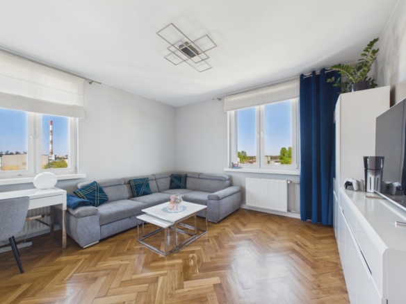 Bright living room with a gray L-shaped sofa, glass coffee table, and blue curtains by large windows. (informative)