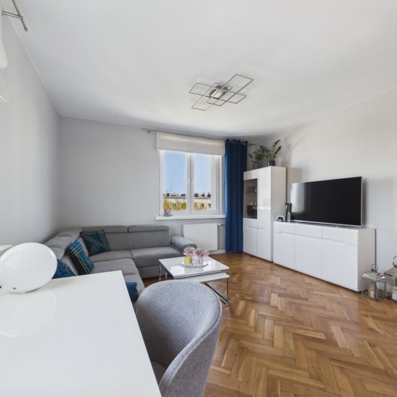 Living room with a gray sectional sofa, white media cabinet, and a flat-screen TV against a light wall.