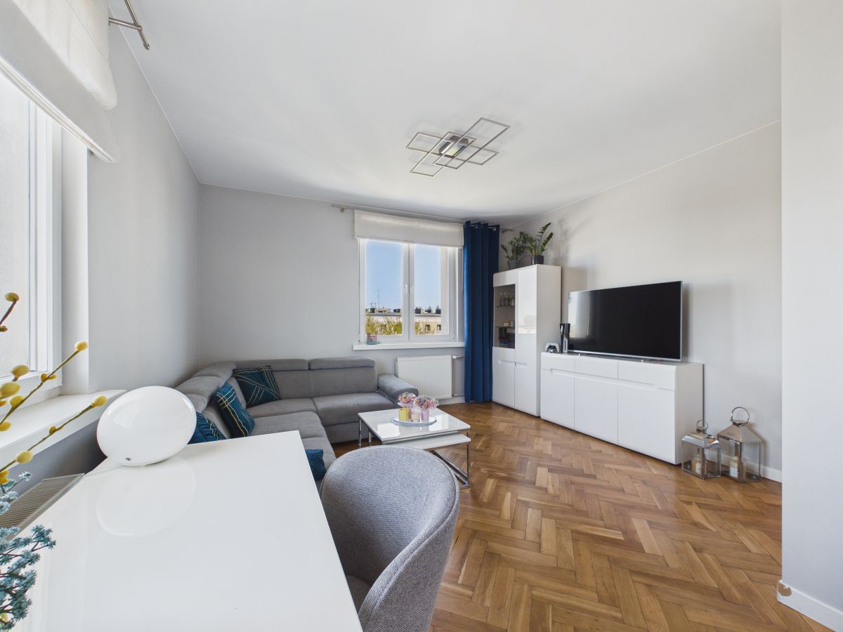 Living room with a gray sectional sofa, white media cabinet, and a flat-screen TV against a light wall.
