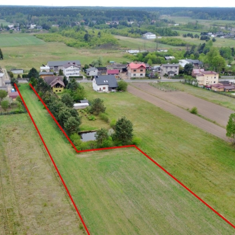 Aerial view of a rural neighborhood with a long narrow property outlined in red along backyards and a road.
