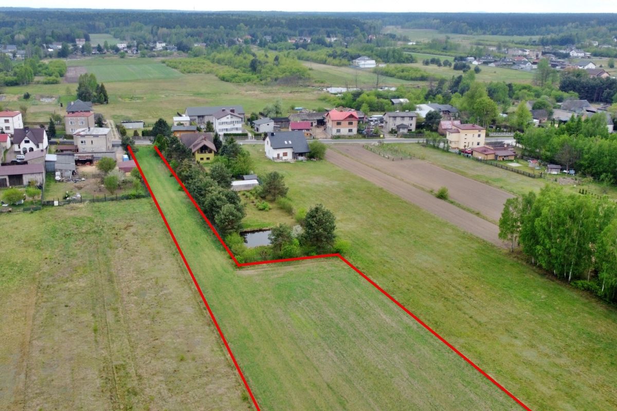 Aerial view of a rural neighborhood with a long narrow property outlined in red along backyards and a road.
