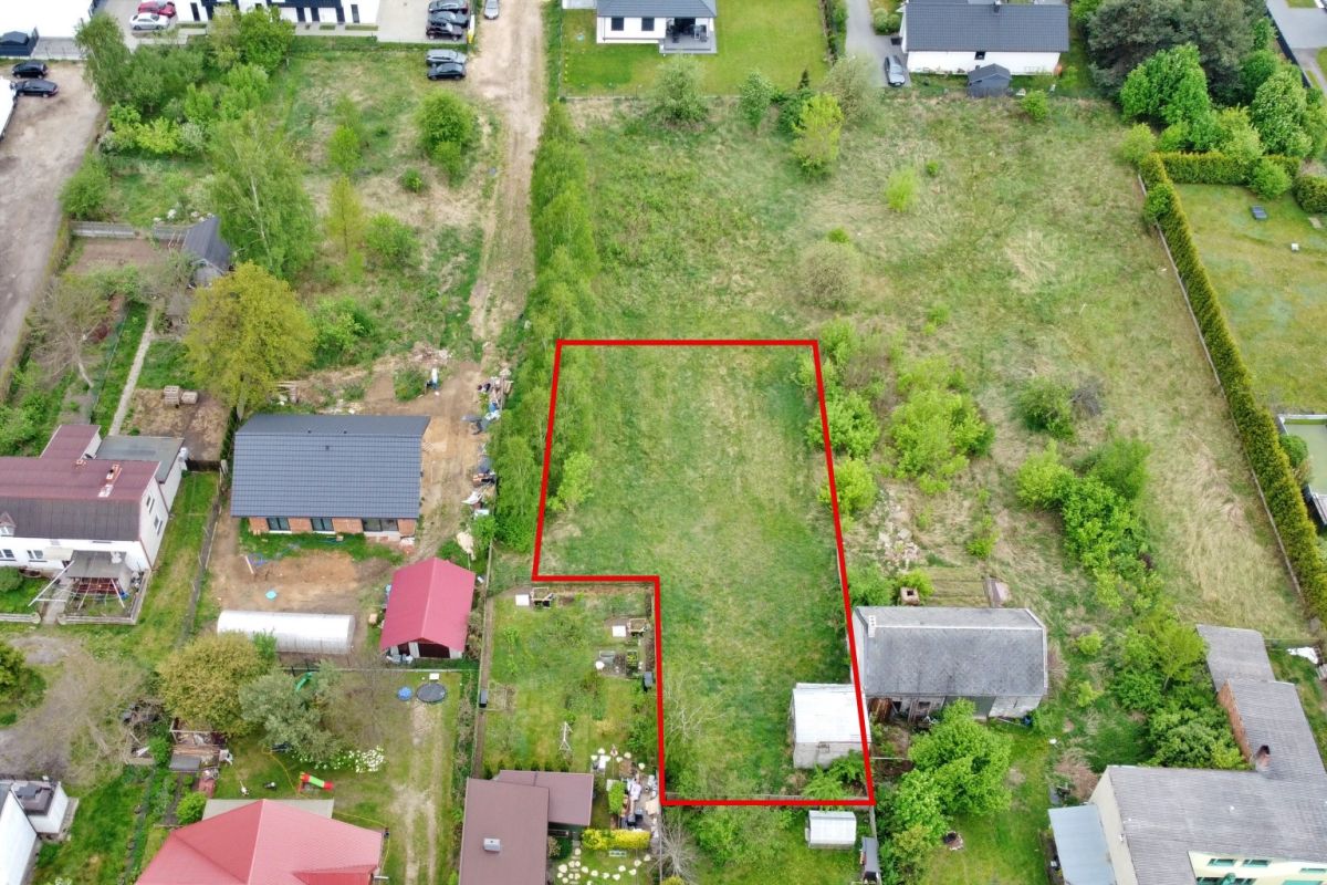 Aerial view of a vacant residential lot outlined in red, bordered by houses and trees in a neighborhood setting.