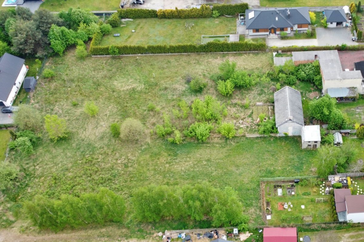 Aerial view of a suburban property: a large grassy plot with scattered trees, bordered by houses and gardens nearby.