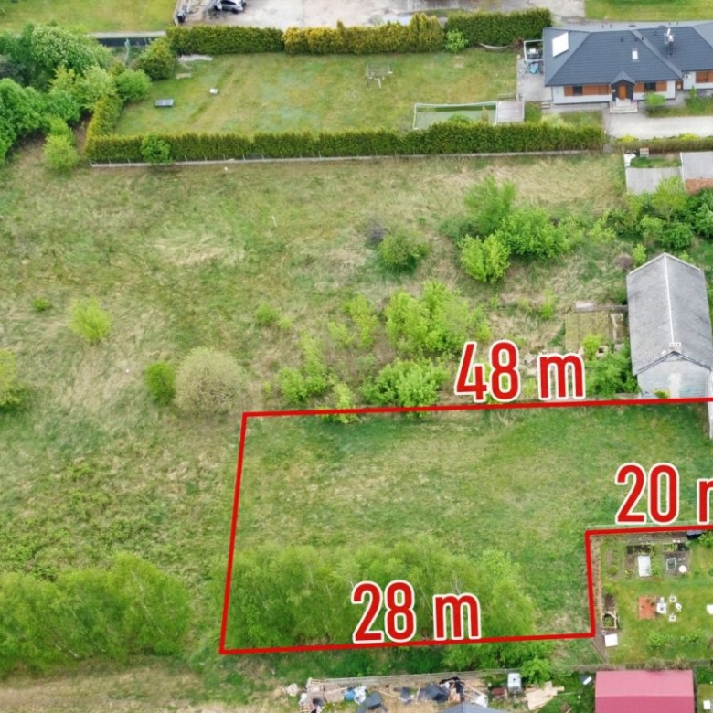 Aerial view of a grassy lot outlined in red with measurements 28 m, 20 m and 48 m, surrounded by trees and houses.