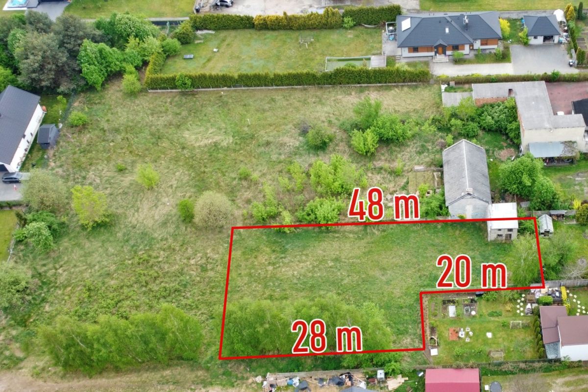 Aerial view of a grassy lot outlined in red with measurements 28 m, 20 m and 48 m, surrounded by trees and houses.