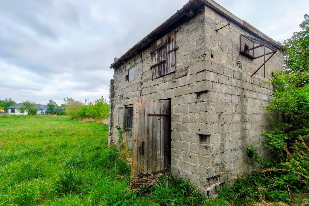 Old concrete outbuilding with a weathered wooden door in a grassy field under a cloudy sky.