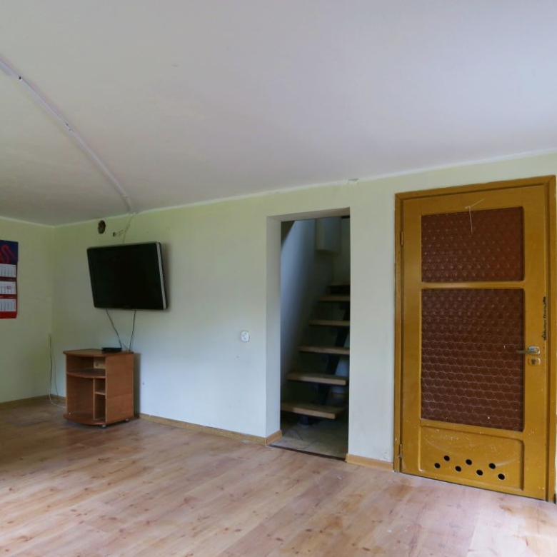 Living room with a wall-mounted TV, small wooden stand, and a doorway to a staircase, flanked by two wooden doors on opposite walls.