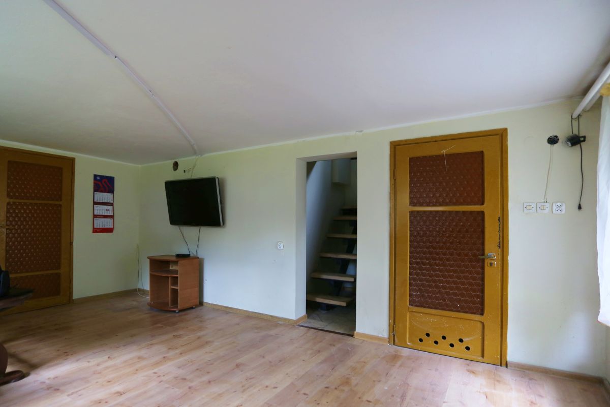 Living room with a wall-mounted TV, small wooden stand, and a doorway to a staircase, flanked by two wooden doors on opposite walls.