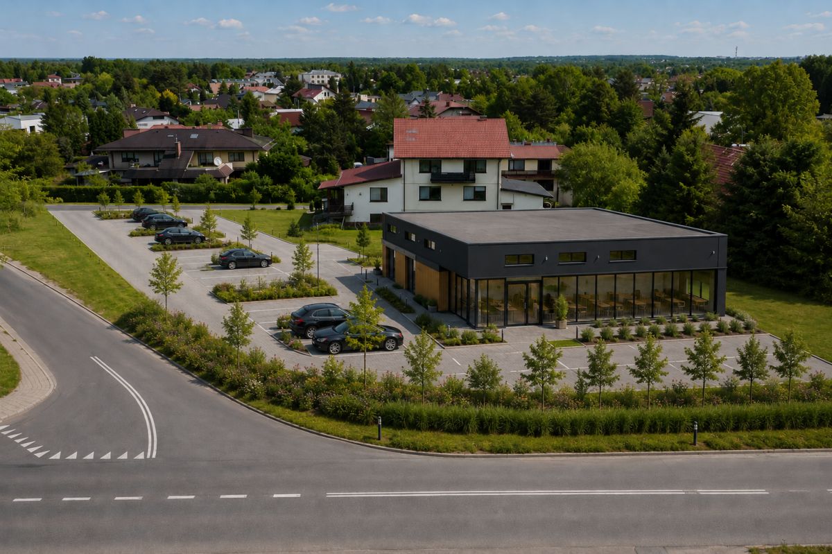 Modern black, glass-front building in a parking lot with landscaped trees in a suburban setting.