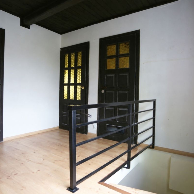 Upper-floor hallway with two black paneled doors and amber glass windows, and a metal railing beside an open stairwell.