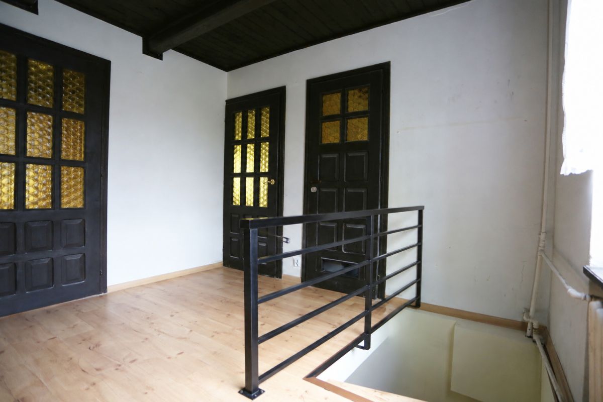 Upper-floor hallway with two black paneled doors and amber glass windows, and a metal railing beside an open stairwell.