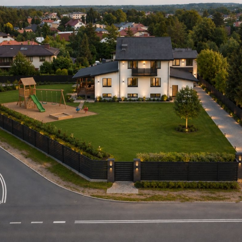 A modern two-story white house with a spacious fenced yard, playground set, and manicured lawn at dusk, adjacent to a quiet street.