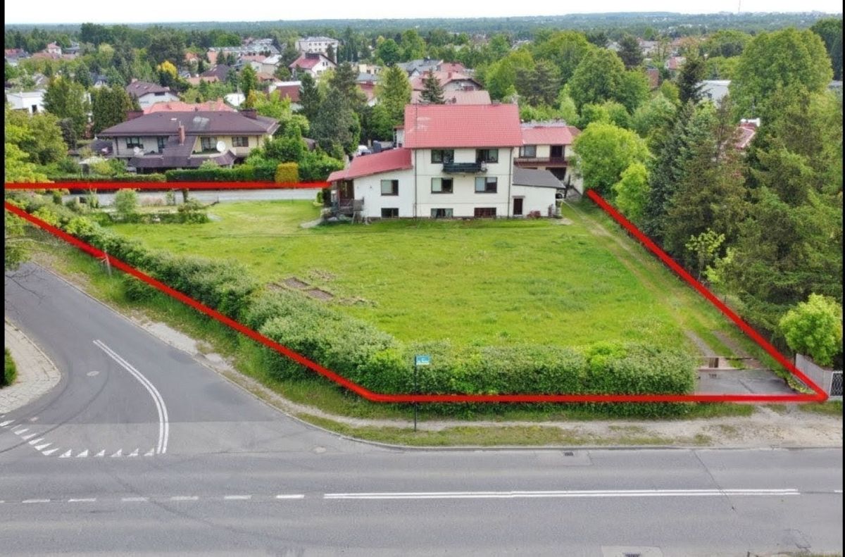 Rectangular grassy property boundary outlined in red along a residential street, with a two-story white house near its center and green trees surrounding it.