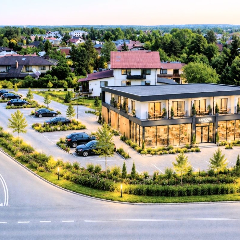 Modern glass-front commercial building labeled Landova, with a parking lot and lush landscaping in a suburban complex.