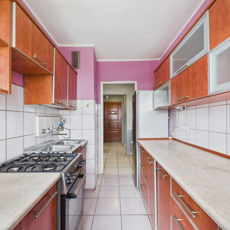 Long narrow kitchen with purple walls, wooden cabinets, and white tiled backsplash; stainless stove and spacious countertops on both sides