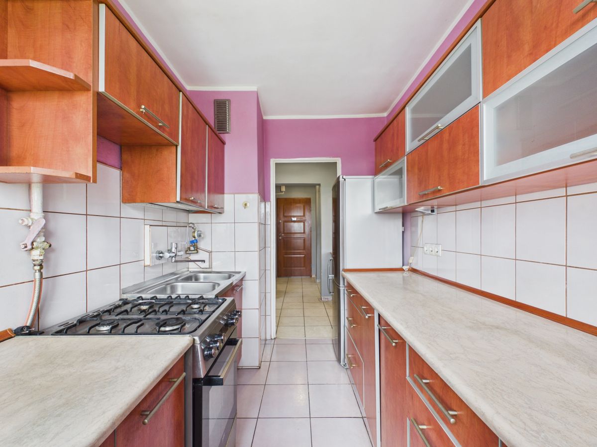 Long narrow kitchen with purple walls, wooden cabinets, and white tiled backsplash; stainless stove and spacious countertops on both sides
