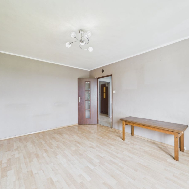 Empty living room with light wood flooring, beige walls, a wooden bench along the right wall, and a glass-front cabinet on the left.
