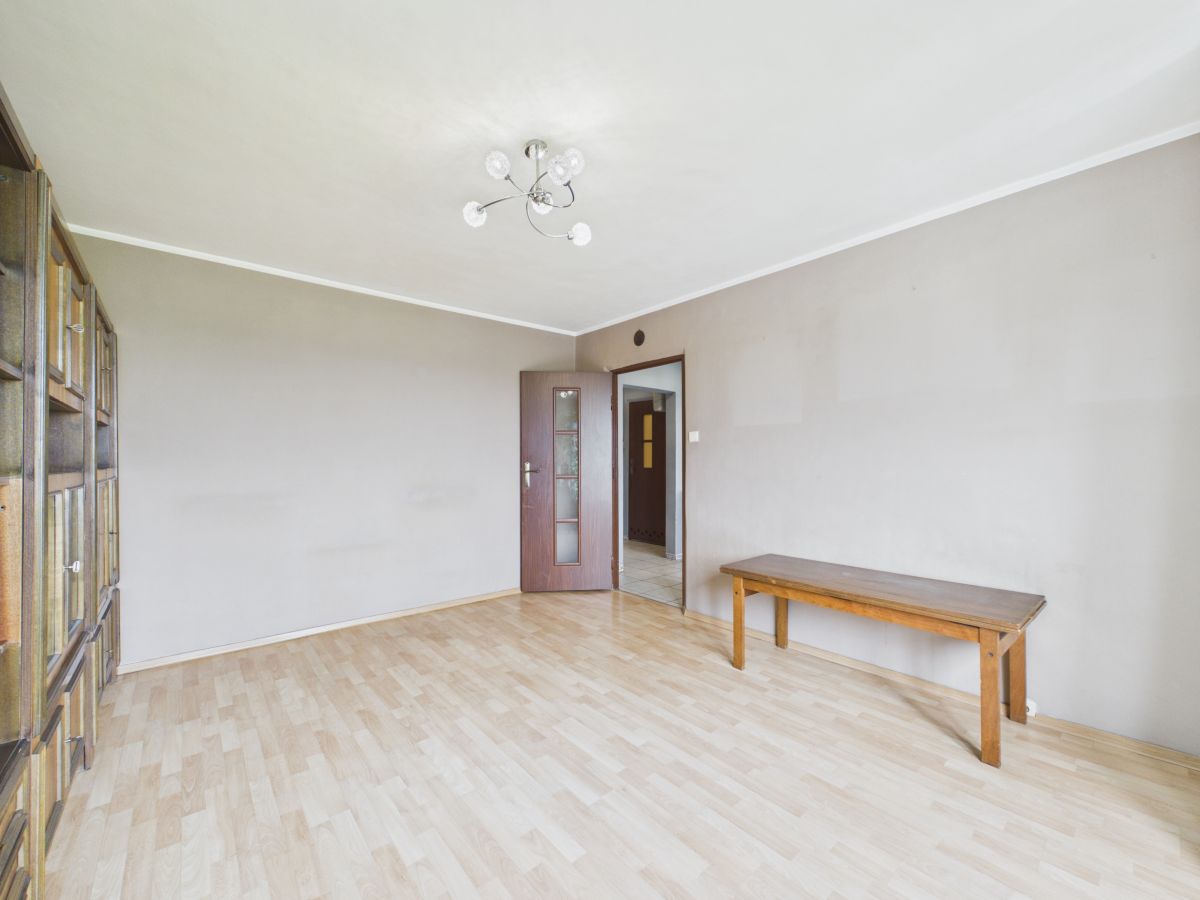 Empty living room with light wood flooring, beige walls, a wooden bench along the right wall, and a glass-front cabinet on the left.