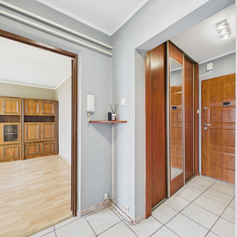 Hallway with tiled floor and wooden doors; view into a room with built-in wooden cabinets along the wall.