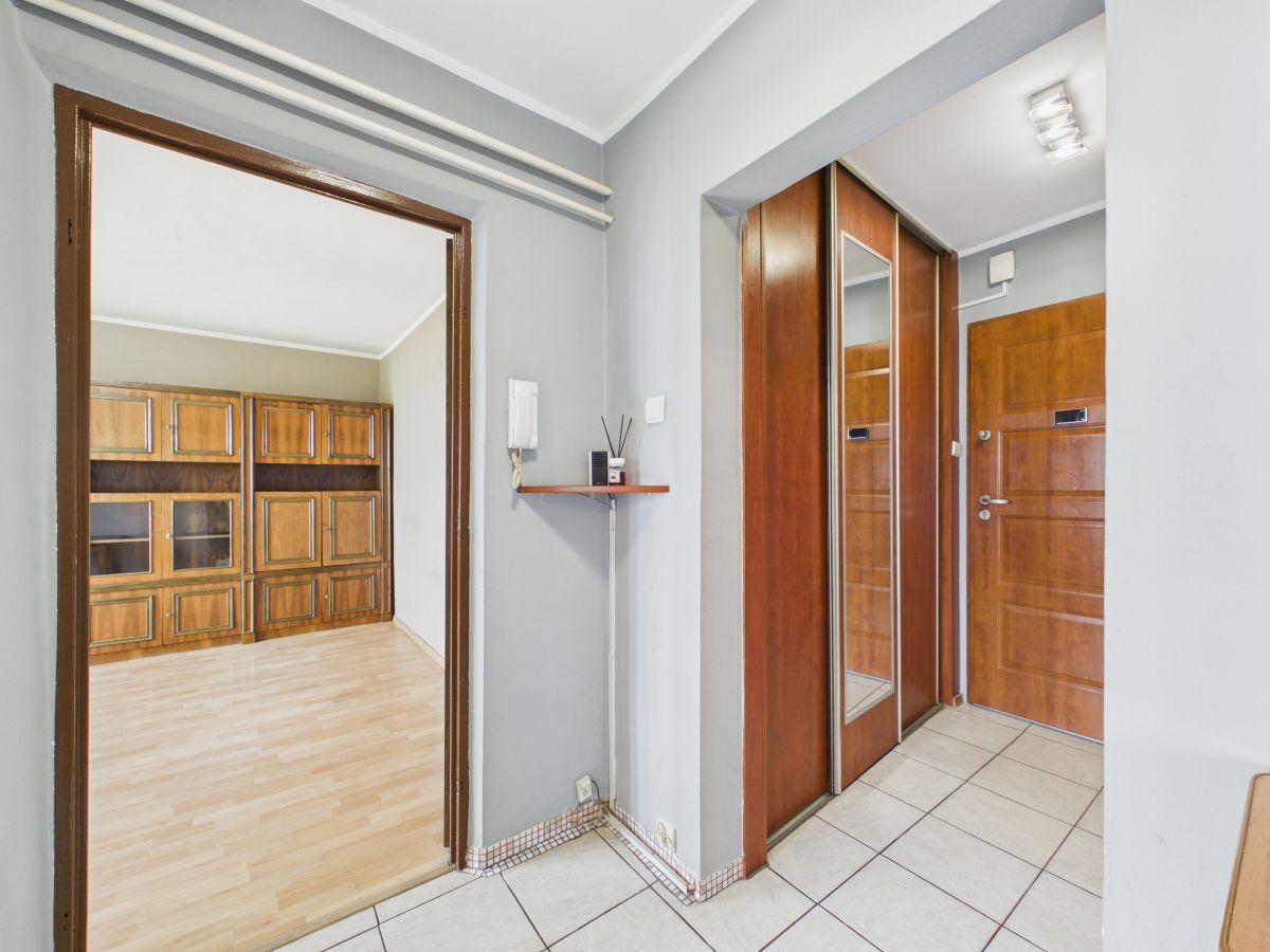 Hallway with tiled floor and wooden doors; view into a room with built-in wooden cabinets along the wall.
