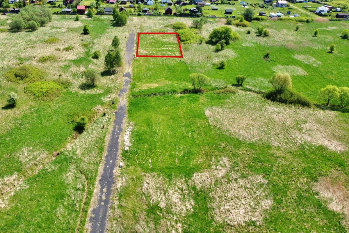 Aerial view of a green rural field with a rectangular plot outlined in red near a dirt road.