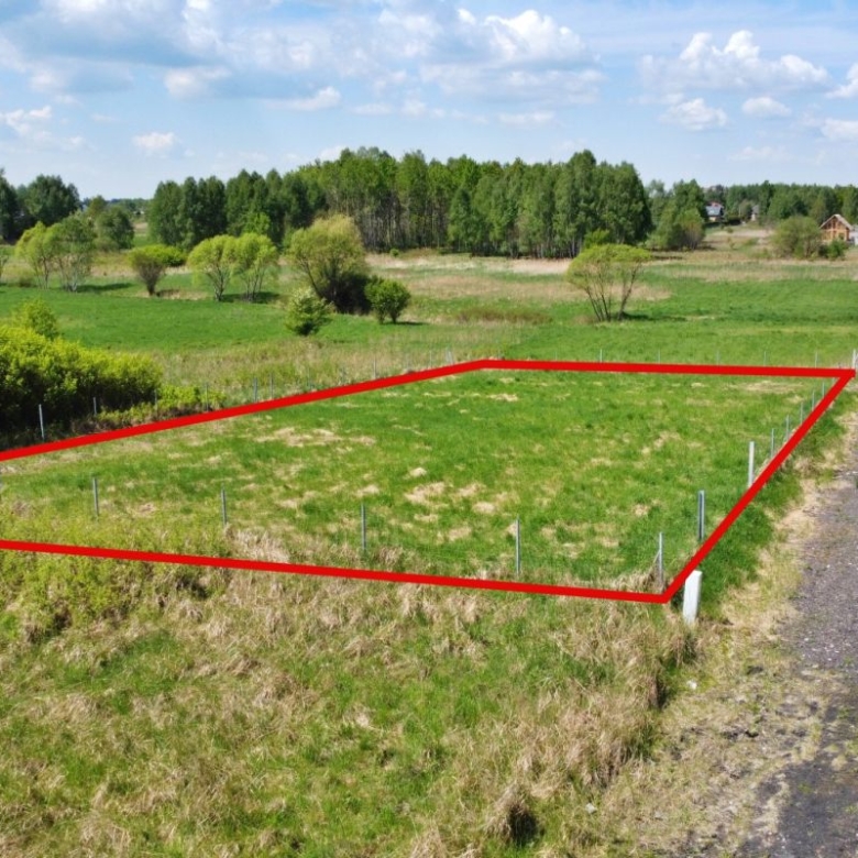 Rectangular grassy lot bordered by red boundary lines and fence posts, beside a gravel rural road.