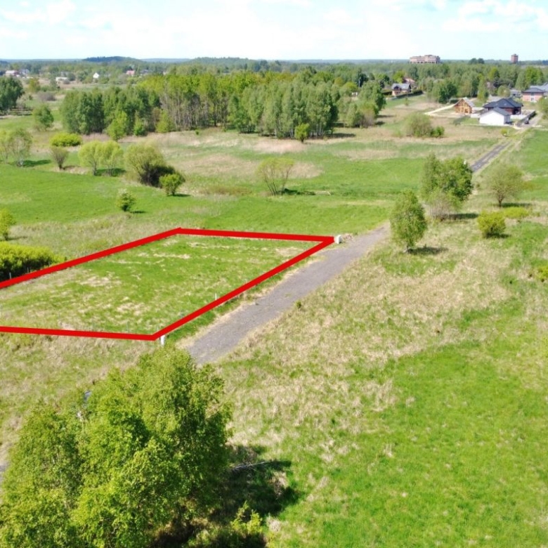 Outline of a rectangular plot of land marked in red along a rural road, surrounded by green fields and scattered trees for sale or development.
