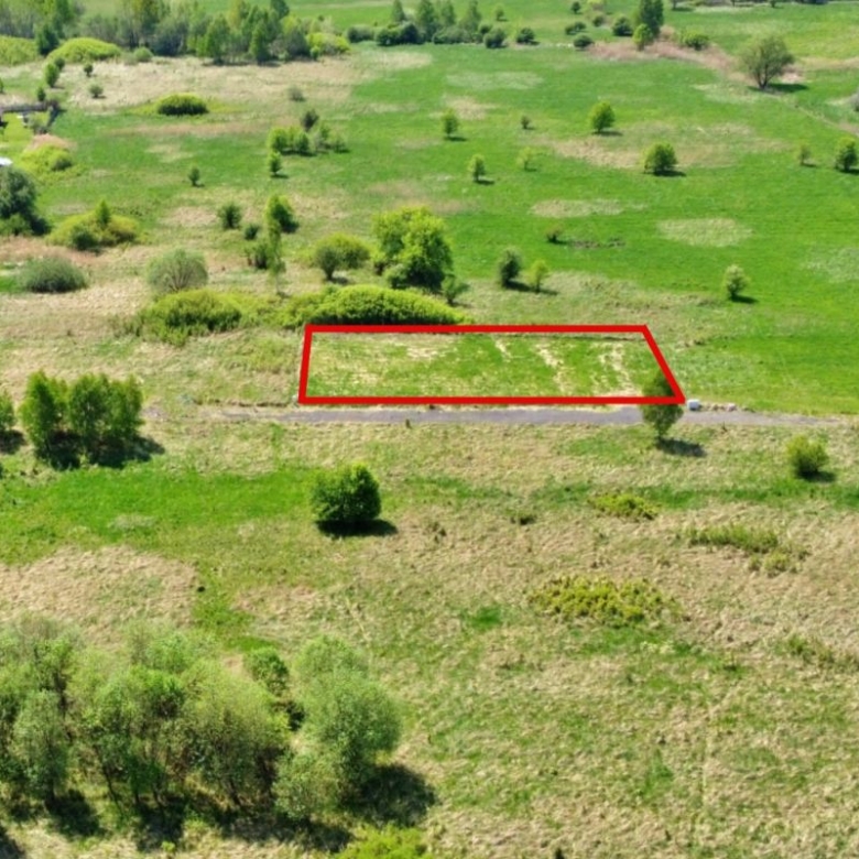 Aerial view of a green countryside with a red-outlined rectangular plot along a road.