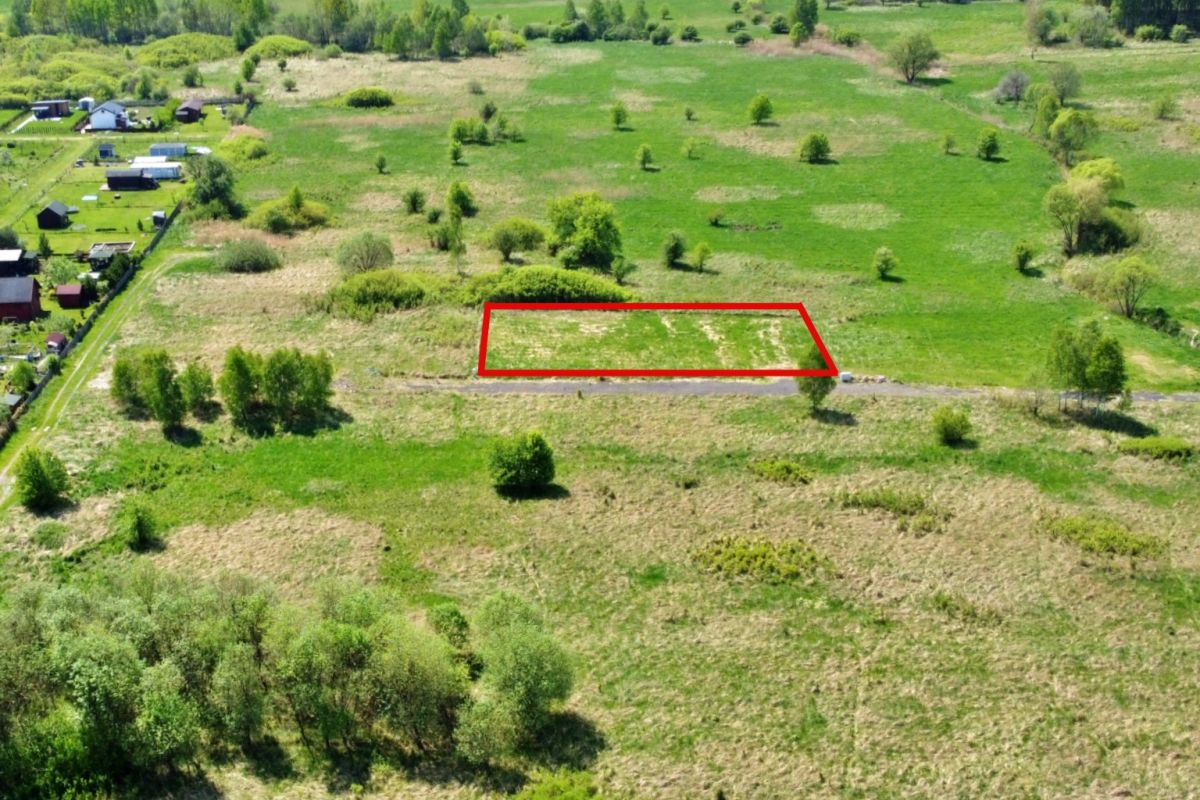 Aerial view of a green countryside with a red-outlined rectangular plot along a road.