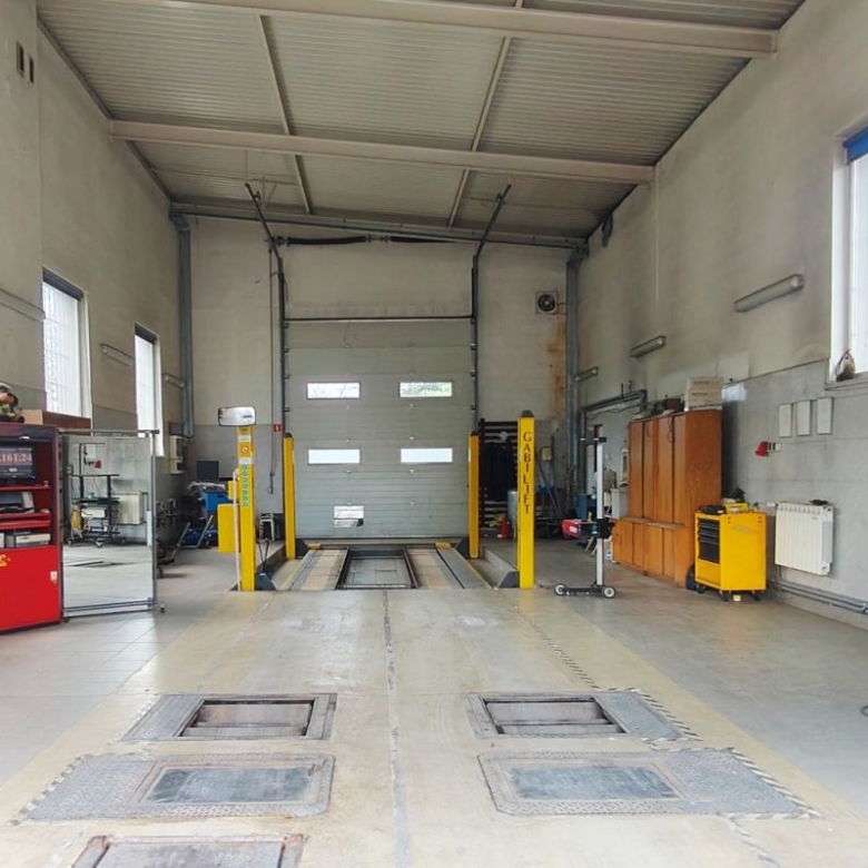 Industrial car workshop with two yellow vehicle lifts, a large roll-up door, and tools along the walls for vehicle maintenance.