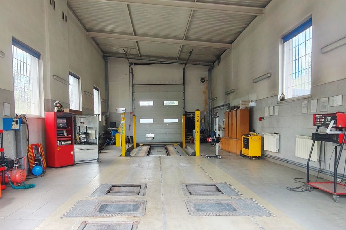 Industrial car workshop with two yellow vehicle lifts, a large roll-up door, and tools along the walls for vehicle maintenance.
