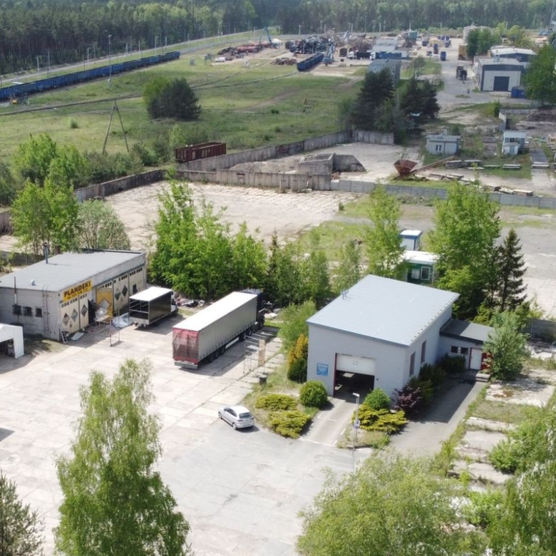 Aerial view of an industrial yard with loading docks, several trucks, a small office building, and surrounding trees.