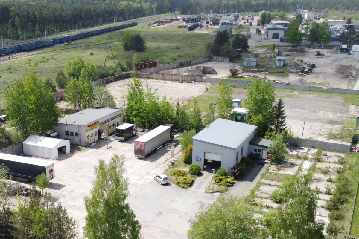 Aerial view of an industrial yard with loading docks, several trucks, a small office building, and surrounding trees.