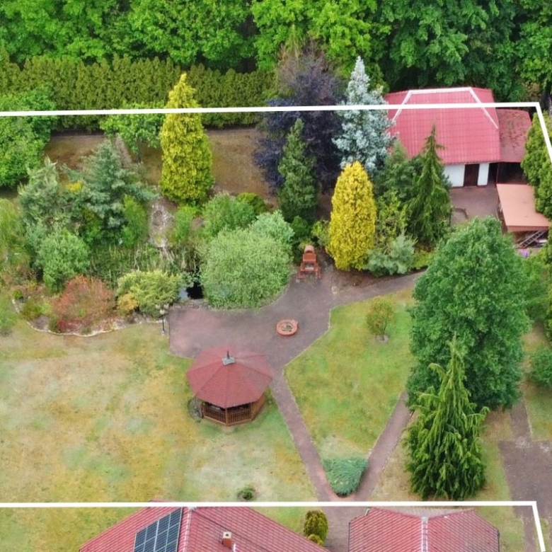 Aerial view of a residential backyard with a gazebo, winding paths, and dense trees inside a white-outline property boundary.