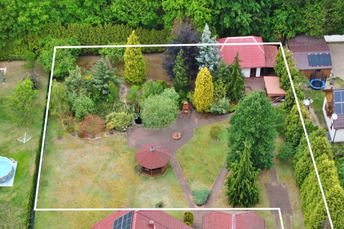 Aerial view of a residential backyard with a gazebo, winding paths, and dense trees inside a white-outline property boundary.