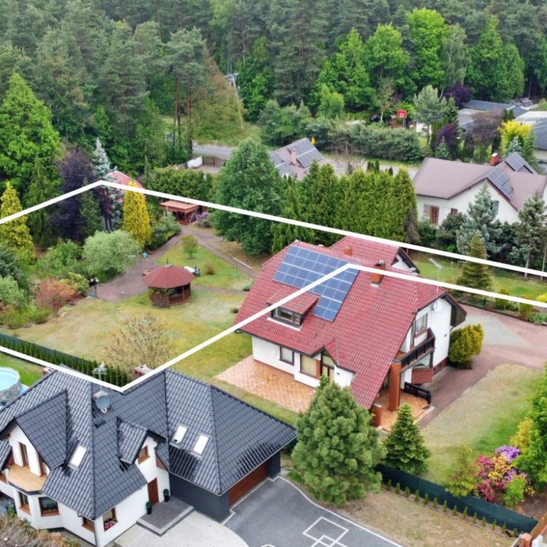 Aerial view of a residential property with white boundary lines marking lot edges; houses, garden, trees, solar panels on the roof, and a circular pool visible in the yard.