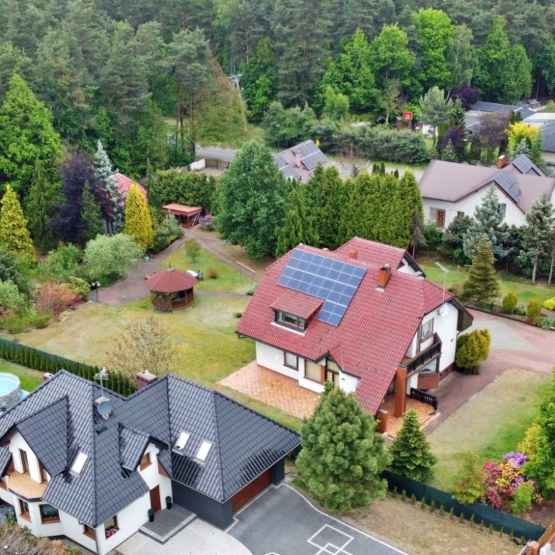 Aerial view of a suburban neighborhood with two modern houses, green yards, and solar panels on one red-roofed house, plus a circular pool in the yard nearby.