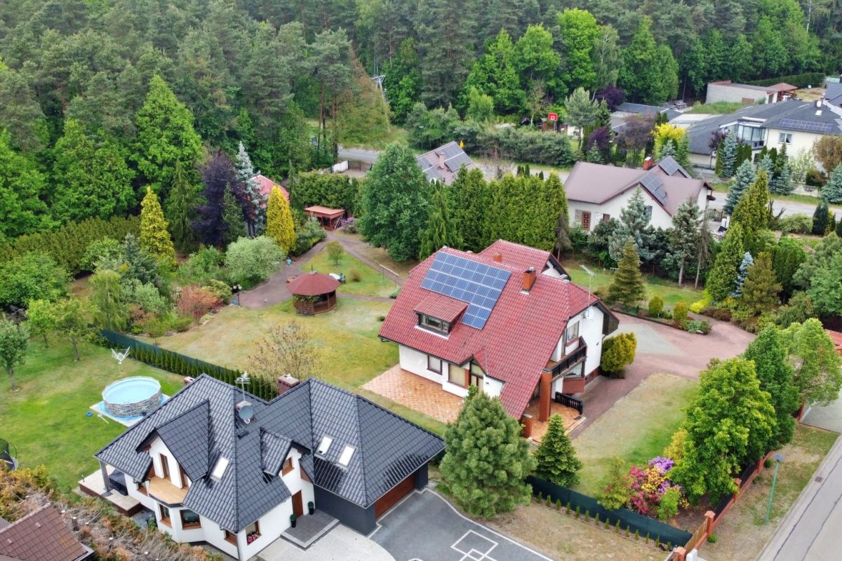 Aerial view of a suburban neighborhood with two modern houses, green yards, and solar panels on one red-roofed house, plus a circular pool in the yard nearby.
