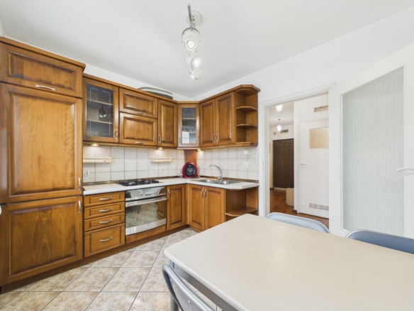Kitchen with dark wood cabinets, tiled backsplash, and a stainless steel oven; a dining table and chairs in the foreground.