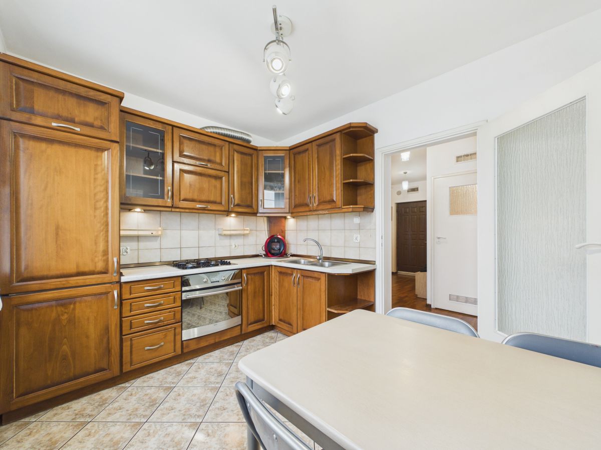 108368789.jpg Kitchen with dark wood cabinets, tiled backsplash, and a stainless steel oven; a dining table and chairs in the foreground.