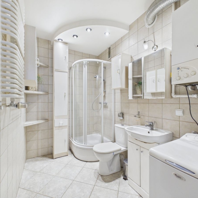 Small modern bathroom with a curved glass shower enclosure, toilet, sink, storage cabinets, and a washing machine on the right.