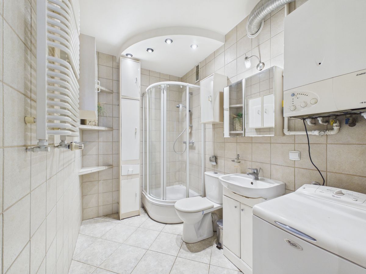 Small modern bathroom with a curved glass shower enclosure, toilet, sink, storage cabinets, and a washing machine on the right.